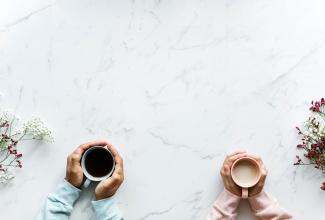 Closeup of two sets of hands holding coffee mugs