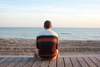 Man seated on boardwalk staring at ocean