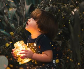 Child holding jar full of fireflies staring up into sky