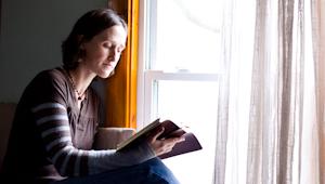 a woman reading a Bible next to a sunlit window