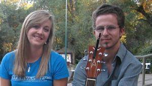 Young woman smiling seated on bench next to young man with guitar