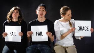 Three young people sitting holding signs. Two wearing black T-shirts hold up signs with "Fail" written on them. The third woman is wearing white holding a sign that says "Grace."