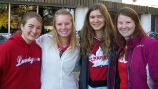 Group of four young female students arm in arm smiling outside of dorm