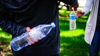 Person handing someone a bottle of water while holding another bottle behind back