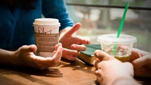 Closeup of two people's hands holding coffee tumblers on table