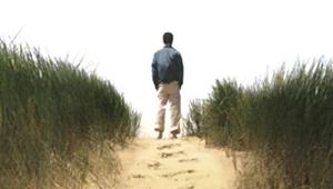 Back of young man staring off into the distance on beach with footprints in sand