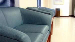 A gray leather couch sitting in a hallway with smooth concrete floors.