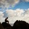student sitting on a rock near the water with the backdrop of a blue sky with white clouds