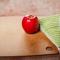 Red apple on cutting board next to kitchen knife on towel