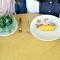 Two people sitting at a table. One has a salad, and the other has a twinkie on a plate.