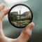 Hand holding camera lens focused on cross with blurry background