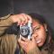 A young black woman holding a camera over her right eye