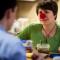 Middle-aged woman wearing red clown nose talking to man across table