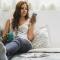 a woman resting on a bed holding a water bottle and looking at her phone