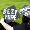 Two college graduates in cap and gown with "Best Friends Forever" written on their caps