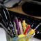 a variety of colorful pens in a cup resting in front of a computer keyboard