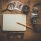  A pencil on white notebook near eyeglasses and a camera