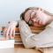 Young woman taking nap on stack of books on top of desk