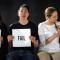 Three young people sitting holding signs. Two wearing black T-shirts hold up signs with "Fail" written on them. The third woman is wearing white holding a sign that says "Grace."