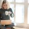 a girl seated cross-legged by a sunny window, holding a mug and using her laptop