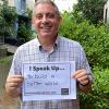 Man smiling and holding a sign that says "I speak up...to build a better world"
