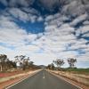 Highway running through rugged landscape with scattered trees and swathes of white clouds