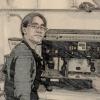 Sepia, edited photo of young man working as a barista with apron and glasses, standing in front of cappuccino machine