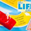 A plastic red car on the board from the board game "Life", and the words "The Life Ahead"