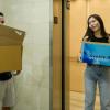 Two students moving into dorm, holding cardboard boxes