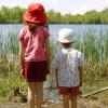 two children, one tall and one short, standing side-by-side and looking out over a lake
