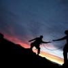 Silhouettes of two people climbing mountain at twilight