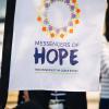 A white sign reading "Messengers of Hope: The University in God's Story"