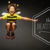Young child in bee costume in midair, grinning, with the words "The Beatitudes" in the background.