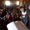 An African woman reading a Bible to a crowded room of listeners