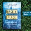 Book cover of Race & Place (blue image of cityscape) laid out on the grass with label: Summer Reading Guide 2017