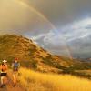 Two people hiking up a trail with cloudy sky and rainbow