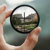 Hand holding camera lens focused on cross with blurry background