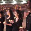 Group of students wearing black holding candles with much larger group in the background in stadium seating