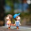 A boy and girl plastic figurine sitting on a tiny park bench and facing opposite ways