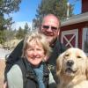 a man, woman, and dog smiling in front of a red barn