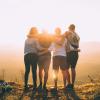 Four friends standing arm in arm and facing a sunset