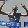 Wesley Korir breaking through tape at Boston Marathon smiling, holding up index finger