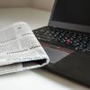 A newspaper resting on the corner of an open laptop computer