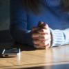Person seated at table with hands folded next to a smartphone