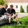 Two male students sitting on a bench on campus talking