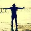 a silhouetted person standing by the water with arms open wide