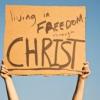 Hands of person holding cardboard sign with the words "Living is Freedom through Christ"