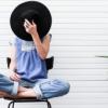woman sitting cross-legged with a wide-brim hat covering her face