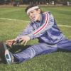 Person on soccer field in bright purple tracksuit grimacing as she stretches