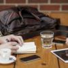 two pairs of hands resting on a wooden table with cups and an iPad on it.